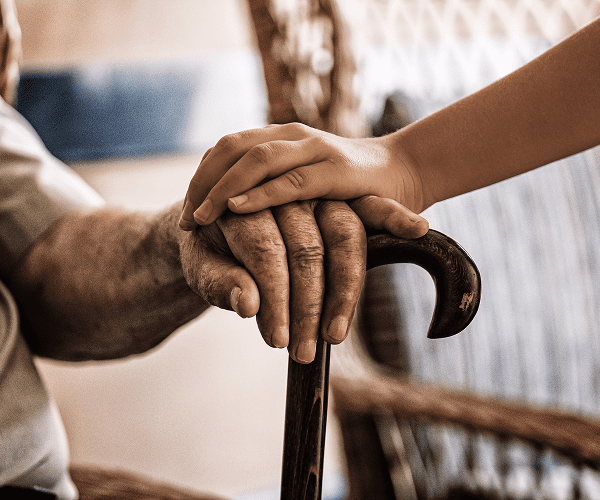 A young person gently holding the hand of an elderly person with a cane, symbolizing care and support at a hospice or care facility.